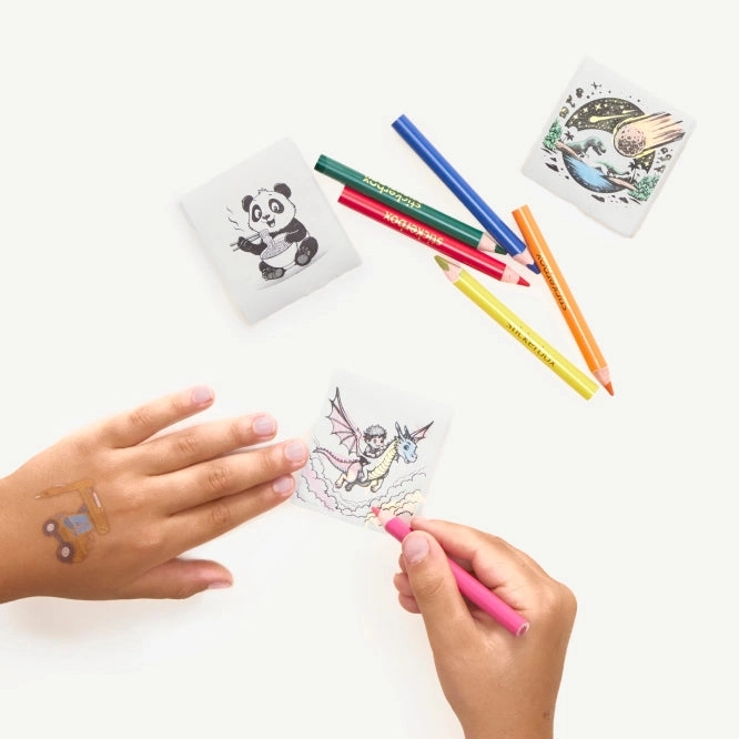Hands peeling and coloring printed stickers next to a row of colored pencils