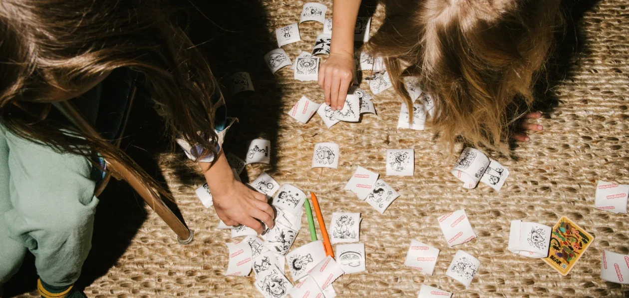 Kids' hands sorting dozens of printed stickers spread across a rug